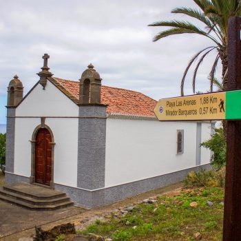 Foto de una iglesia y un cartel que señala la Playa Las Arenas y el mirador Barqueros