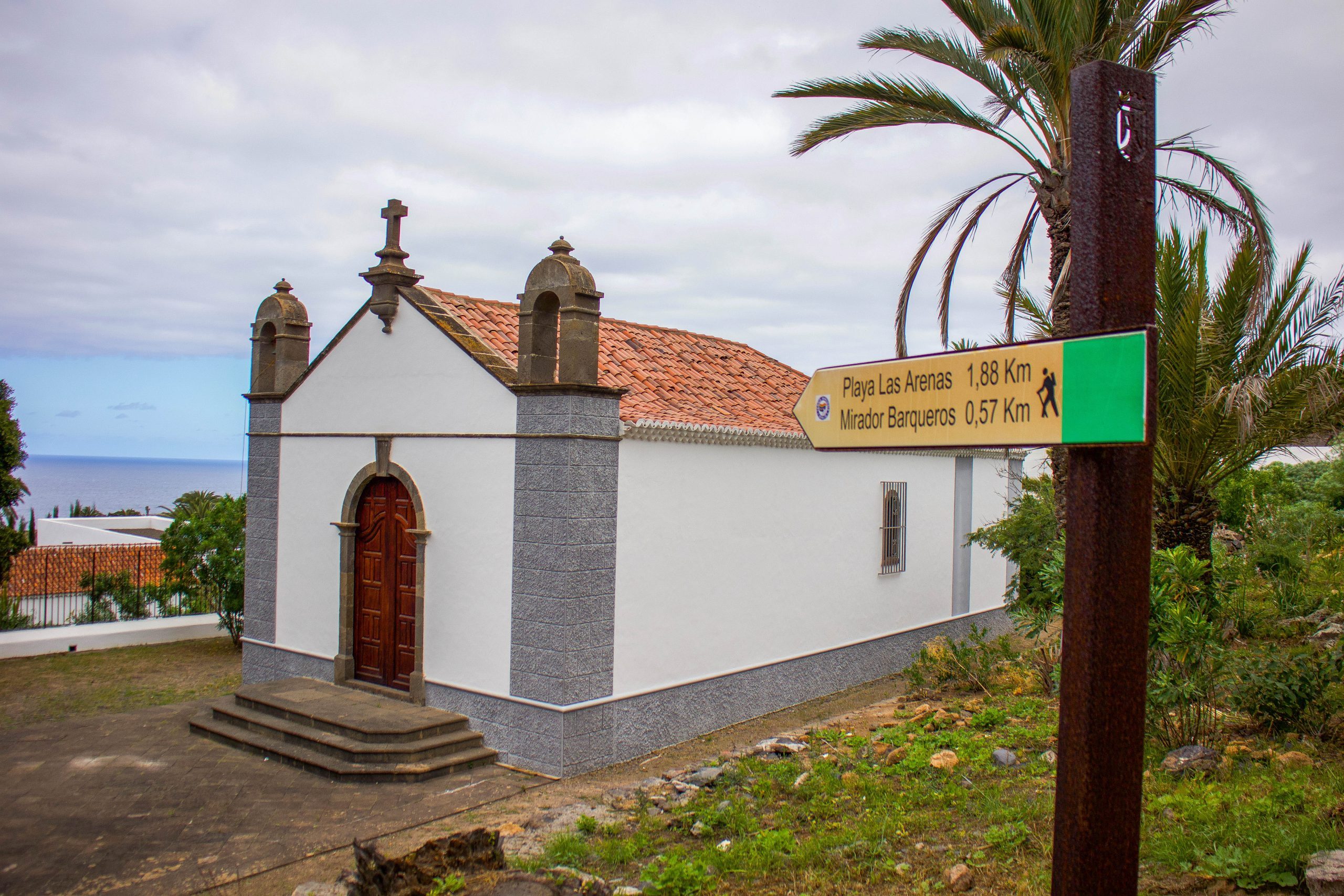 Foto de una iglesia y un cartel que señala la Playa Las Arenas y el mirador Barqueros